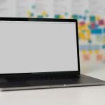 A laptop on a table with a blank screen in front of a wall filled with colorful sticky notes.