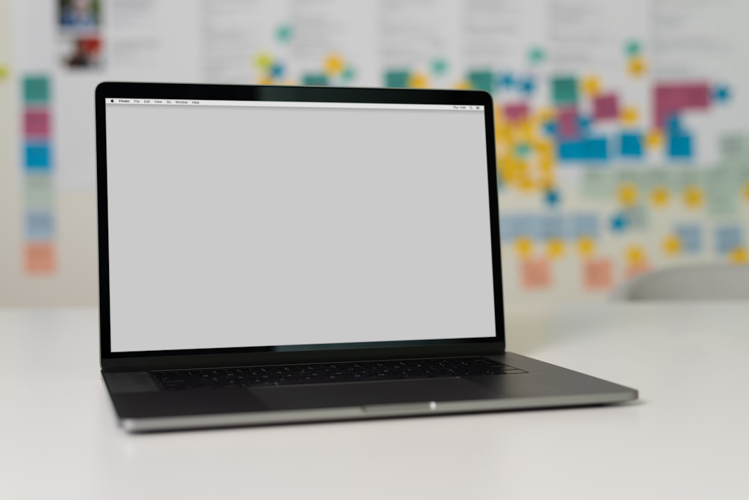 A laptop on a table with a blank screen in front of a wall filled with colorful sticky notes.