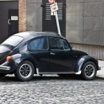 An old black car parked on a cobblestone street near a modern building.
